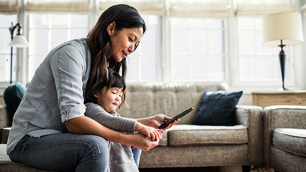 Woman and little girl look at a tablet together in their living room